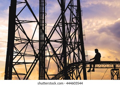 Silhouette, high voltage tower, telecommunication tower, TV antennas with worker repairing, maintenance in sunset