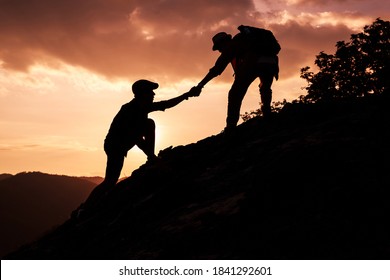 Silhouette of hiker helping each other hike up a mountain at sunset. - Shutterstock ID 1841292601
