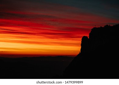A silhouette of a hill with a cross with the orange, yellow and red sky by sunrise