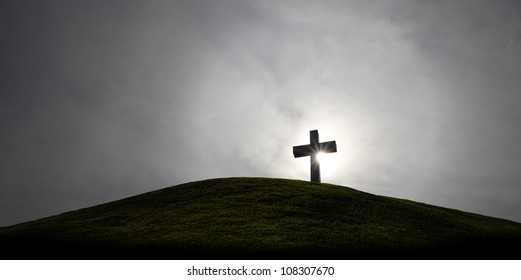 Silhouette of a holy christian crucifix illuminated by sunlight on top of a hill on a dramatic cloudy sky.