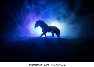 Silhouette of a horse miniature standing at foggy night. Creative table decoration with colorful backlight with fog. Selective focus