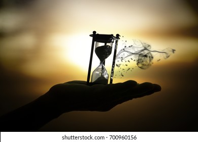 Silhouette hourglass is disintegrating on hand Pocket watch at last sunlight (Concept of wasting time)