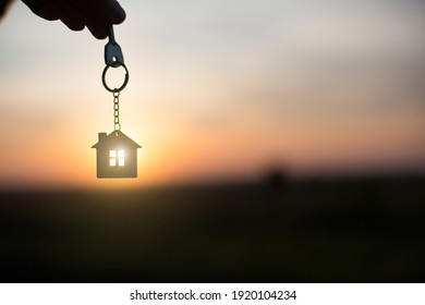 Silhouette of a house figure with a key,  keychain on the background of the sunset. They dream of a house, building, moving to a new house, mortgages, renting and buying real estate. Copy 