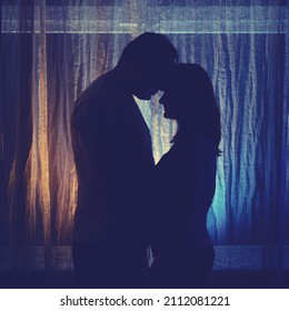 Silhouette Of Hugging Man And Woman At The Night Window. Couple Husband And Wife, Family Love In The Evening Light Of The Home Living Room