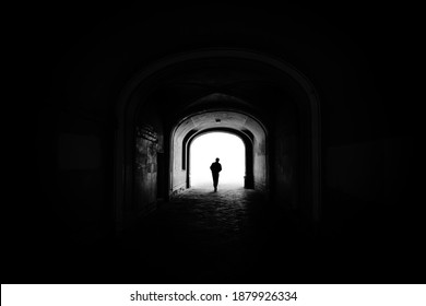 Silhouette of a human figure in a dark tunnel or arch of an old building