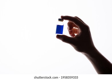Silhouette of human hand, holding little bottle with blue liquid. Isolated, white background, copy space, close up.