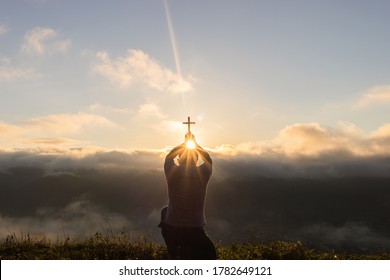 Silhouette of human kneeling down praying and holding christian cross for worshipping God at sunset background. Christian, Christianity, Religion copy space background. 