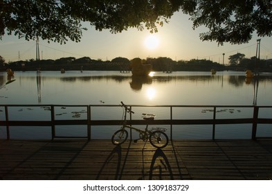 Silhouette Image Of Bicycle At Park Beside Lake With Good Air And No Polution. Sunset Background And Big Duck.