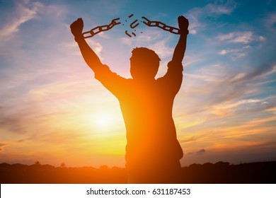 Silhouette image of a businessman with broken chains in sunset.