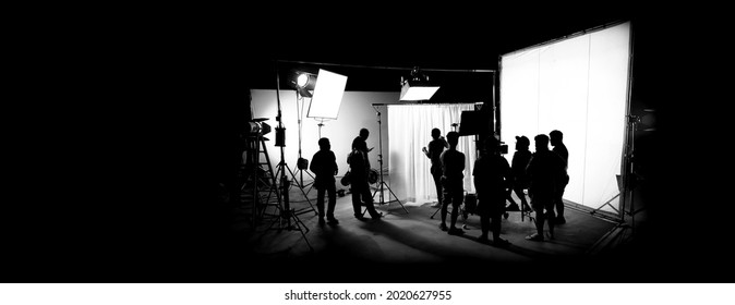 Silhouette Images Of Film Production. Behind The Scenes Or B-roll Of Making Video Commercial Movie. Film Crew Lightman And Cameraman Working Together With Film Director In Studio. Film Industry.