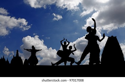 Silhouette of Indian classical dancers posing against Hindu temple against a surreal dramatic cloudy blue sky.