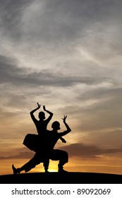 Silhouette of Indian cultural classical dancer posing on a hill against a surreal dramatic sunset sky.