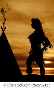 a silhouette of a Indian woman by her teepee, with the wind blowing.