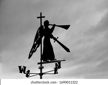 Silhouette Of Iron Trumpeting Angel With Sword And Trumpet. Weather Vane On Roof Of House. Blue Sky Background. Christian Angel Of The Apocalypse