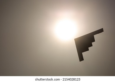 silhouette of isolated stealth bomber against bright sun and sky, in monochrome