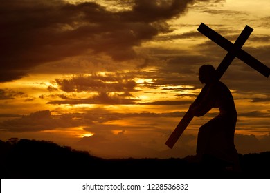 Silhouette of Jesus christ carrying cross over sunset background