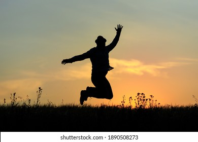 silhouette of a joyful adult man in a hat who jumps with happiness against the background of the evening sky. sunset and joy at the end of the day