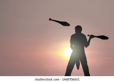 Silhouette Of A Juggler Performing His Juggling Act At Sunset.  