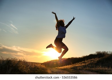 Silhouette Of Jumping Woman On Sunset Sky Background