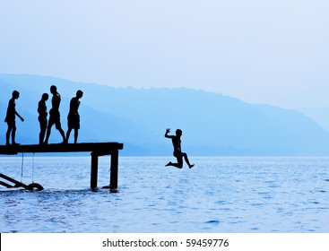 Silhouette Of Kids Fun On Lake Docks.