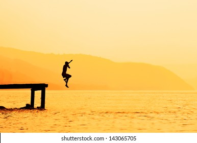 Silhouette Of Kids Jumping From River Dock, At Sunset.