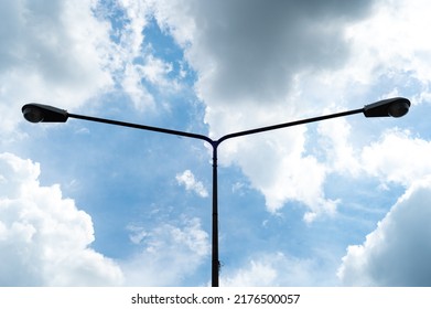 Silhouette of a lamppost with two lanterns against the background of a bright daytime sky.