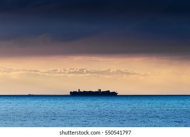 Silhouette Of Large Container Ship On The Horizon Crossing Baltic Sea Under Dramatic Dark Nimbostratus Cloud Formation. Pomerania, Poland.