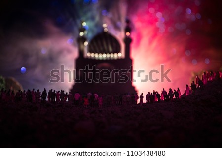 Silhouette of a large crowd of people in forest at night standing against a blurred mosque building with toned light beams on foggy background. Ramadan Kareem background. Praying people concept.