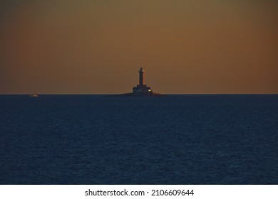 Silhouette Of A Lighthouse And Boat On The Ocean Sea Waters.