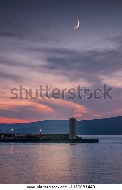 Silhouette of the Lighthouse and
waxing crescent,  first quarter phase of the moon during beautiful
scenic, summer, red sunset in Croatia, Adriatic sea. No
people.