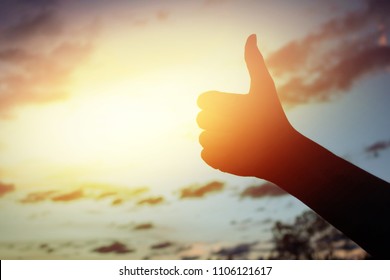 Silhouette like hand symbol thumbs up on meadow in sunset 