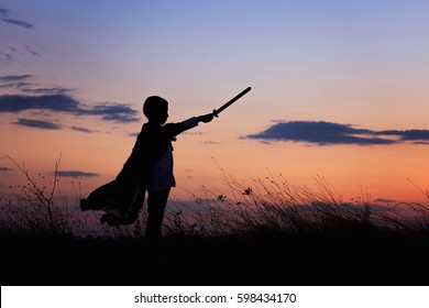 Silhouette of little boy hold toy sword playing on sunset
