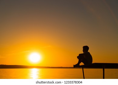 Silhouette of a little boy sitting on the bridge in river at the sky sunset. A lonely boy sits quietly and looks ahead at a beautiful view of sunset.