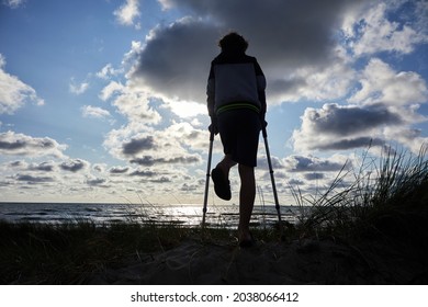 Silhouette of a little boy standing with crutches on the beach.
