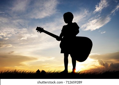 Silhouette a little boy traveling with guitar. Summer, Asian kid at the sunset, happy time, Children who have dreams of being a musician.
