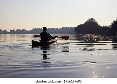 Silhouette Of A Lone Man Kayaking At The Evening Near The Shorelines In Danube River