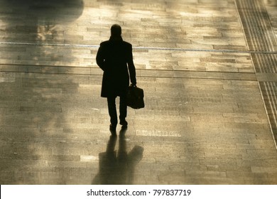 Silhouette of lonely man holding a bag walking ahead back view