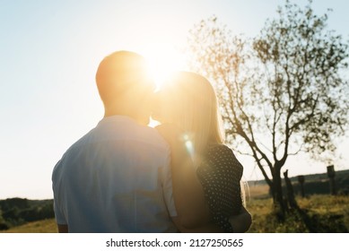 Silhouette love couple kissing, dancing, hugging, flirting together with each other on romantic date at sunset outdoors. Back view of caucasian heterosexual young family against blue sky on sunny day.
