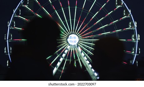 Silhouette Of Love Couple Kissing On Illuminated Ferris Wheel Background Outdoor. Unknown Man And Woman Having Romantic Date At Night In City Center. Unrecognizable Guy And Girl Felling Happy Outside.