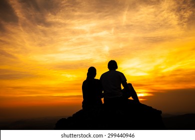 Silhouette of loving couple sitting on a rock in sunset