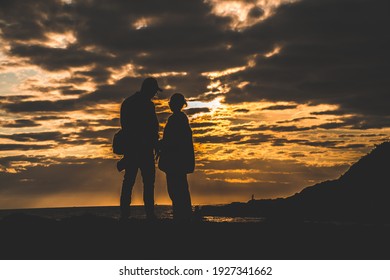 Silhouette of loving couple at sunrise. Man and woman holding hands on the seashore. Love and romance