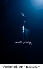 Silhouette Of Mafioso Buttoning Up On Dark Blue Background