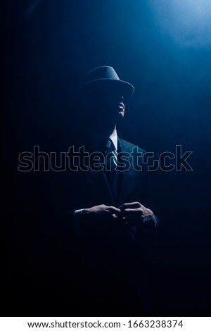 Silhouette of mafioso buttoning up on dark blue background