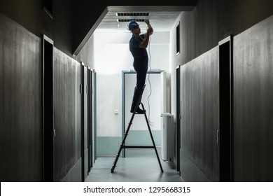 Silhouette Of A Male Electrician On Step Ladder Installing Light At Corridor