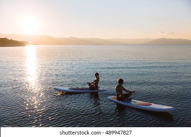 Silhouette of male and female in yoga pose on sup surf swimming at the ocean. Concept lifestyle, sport, love