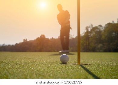 Silhouette male golfer putting golf ball on the green golf, lens flare on sun set evening time.                                - Powered by Shutterstock