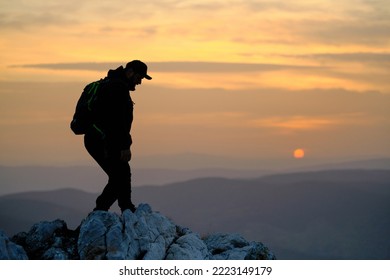 Silhouette Of A Male Hiker On The Rocky Mountain Top Peak At Sunset.