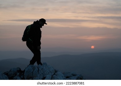 Silhouette Of A Male Hiker On The Rocky Mountain Top Peak At Sunset.