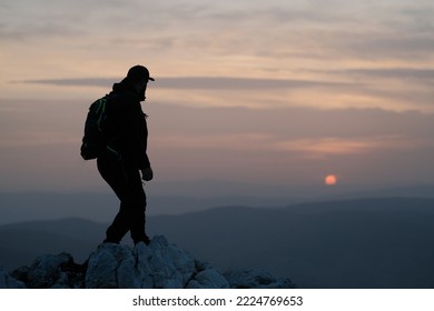 Silhouette Of A Male Hiker On The Rocky Mountain Top Peak At Sunset.