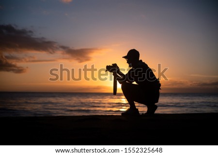 The silhouette of a male hobbyist photographer taking photos of a beautiful colorful sunset on the West Puerto Rico coast near Rincon - a popular beach among tourists year-round.